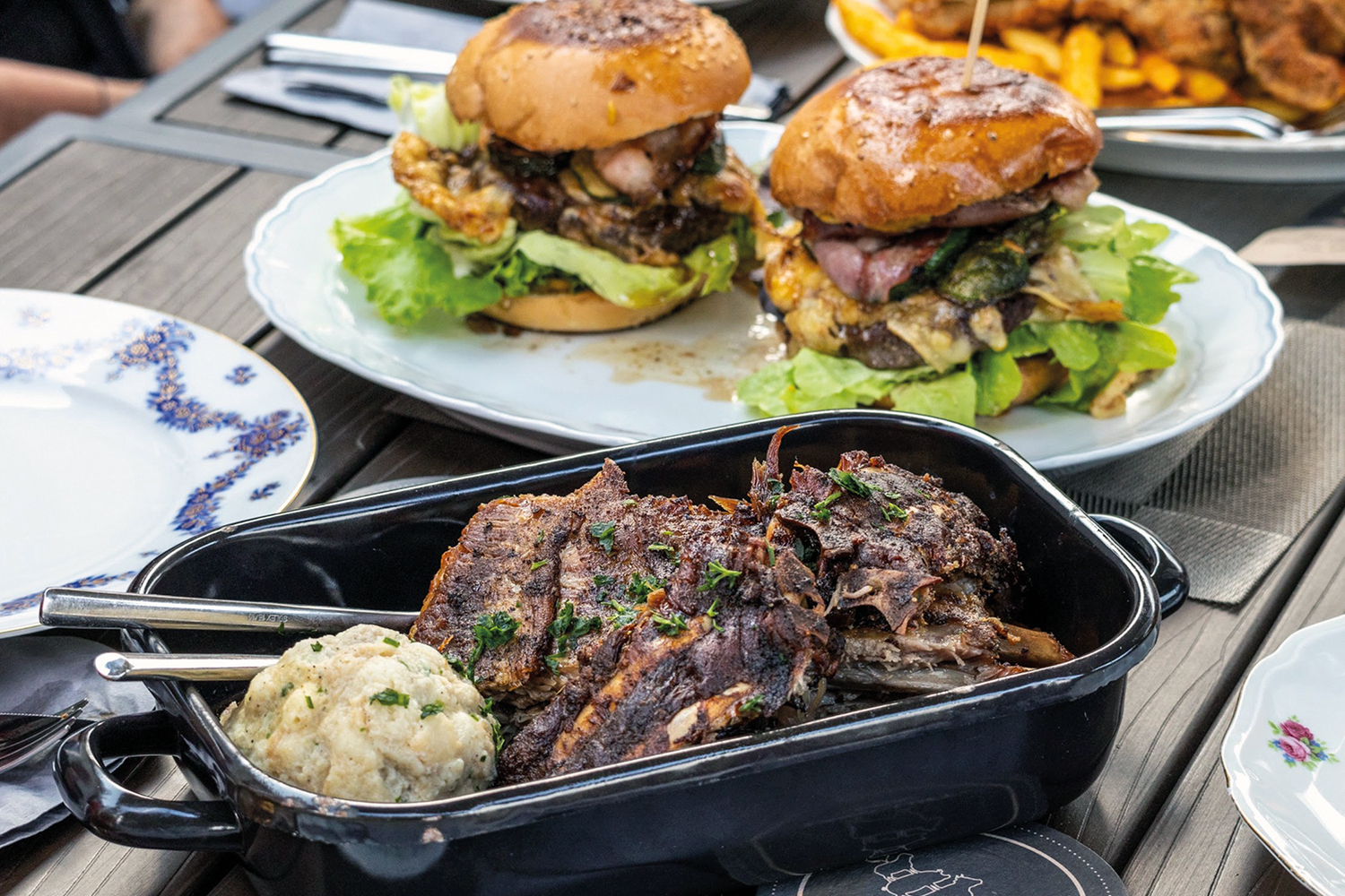 Rein der Mitte mit Braten und Knödel, daneben ein Teller mit zwei Burger
