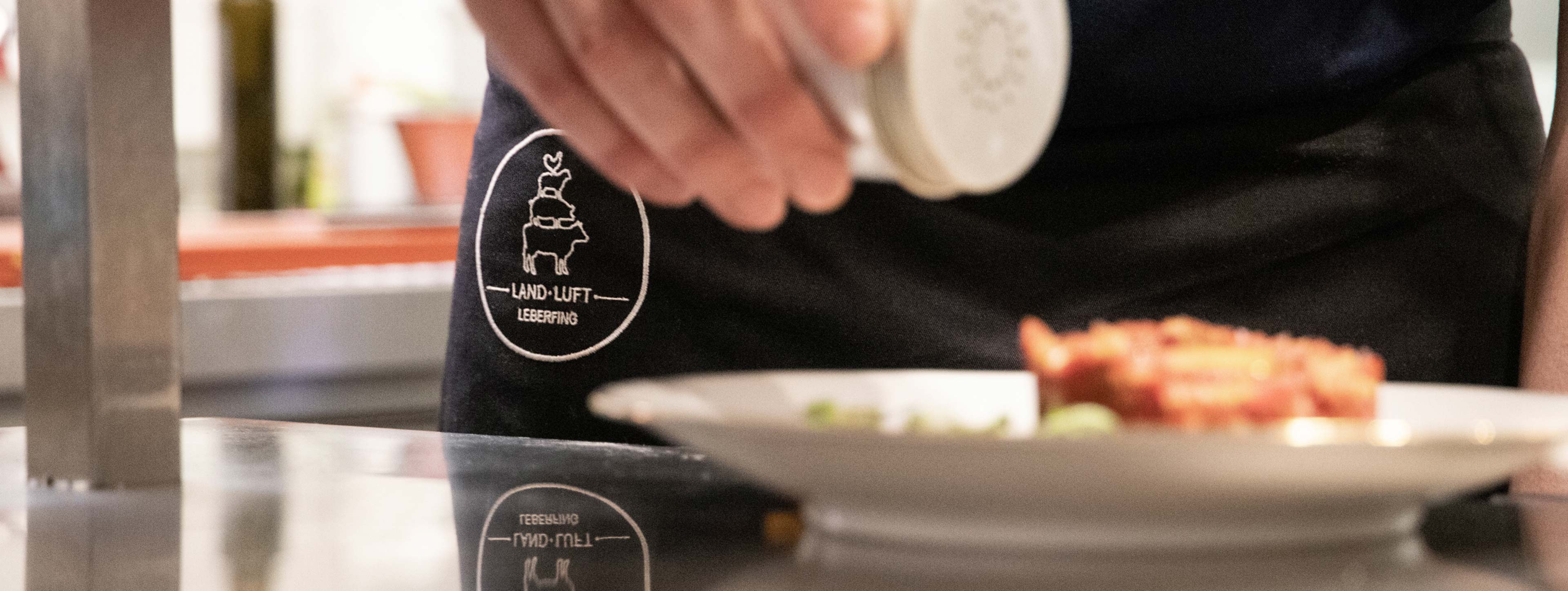 Küchenchef richtet Rindertatar an, Schürze mit Land.Luft Logo